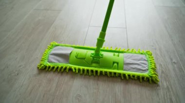 Evde yerde hareket eden mikrofiber ıslak paspas. Yeşil bir fırçayla yerleri paspaslayan terlik giymiş biri. Ev işi. Yakın plan..