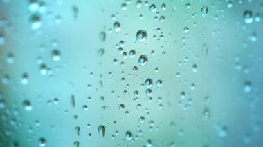 Yağmur damlalarıyla güzel mavi bir zemin. Yağmurlu bir havada cam bir pencerenin üzerine şeffaf su damlaları. Yakın plan..