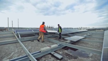 Teknisyenler metal zemine güneş paneli kuruyor. Düz çatıya güneş panelleri kuran iki işçi. PV paneli güneş enerjisini elektrik enerjisine dönüştürür.