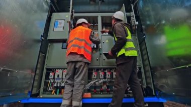 Mühendisler dışarıdaki elektrik sistemine bağlanıyor. Koruyucu üniformalı iki elektrikçi güneş enerjisi santralindeki voltajı kontrol ediyor..