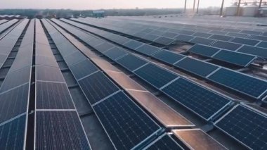 Gün batımında güneş pilleri üzerinde güneş ışığı yansıması. Büyük bir binanın çatısında sıra sıra fotovoltaik paneller bulunan yenilikçi güneş çiftliği. Yenilenebilir enerji kaynağı.