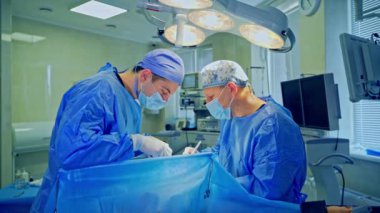 Modern ameliyathanede ameliyat. Tıbbi üniformalı ve maskeli iki doktor yoğun bakım ünitesindeki bir hastaya ameliyat yapıyor..