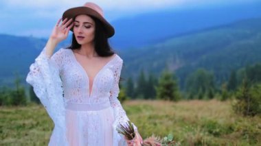 Doğanın arasında beyaz elbiseli romantik bir gelin. Dağ manzarasında gelinlik ve şapka giymiş güzel bir kızın portresi..