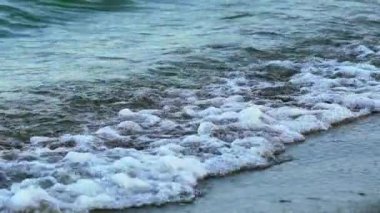Kıyı şeridinde deniz suyu. Dalgalar kıyıya çarpıp köpüklü su yapıyor. Okyanusun kıyısındaki muhteşem manzara. Yavaş çekim.