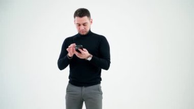 Akıllı telefonlara bakan yaratıcı iş adamı. Beyaz stüdyo arka planında izole edilmiş cep telefonu kullanan siyah kazaklı yakışıklı bir adam..