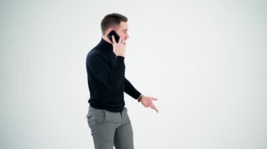 Genç işadamı telefonda konuşuyor. Siyah kazaklı ve gri pantolonlu yakışıklı bir adam cep telefonuyla e-işi yönetiyor. Beyazda izole edilmiş adam.