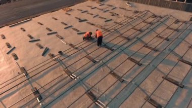 Güneş teknisyenleri çatıda. Bir binanın çatısındaki güneş çiftliğinin gelecekteki fotovoltaik panelleri için metal taban. Hava görünümü.