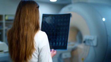 Sıhhiye çağdaş bir klinikte röntgen incelemesi yapıyor. Elinde radyogram resmi olan bir kadın doktorun arka görüntüsü. Tıbbi konsept.