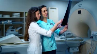 Tıp çalışanları röntgen fotoğrafını tartışıyor. Klinikteki yeni ekipmanların arkaplanındaki röntgen fotoğrafını inceleyen iki kadın doktor..