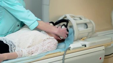 Kadın hasta MRI tarayıcısında yatıyor. Hemşire tomografi çekmeden önce hastayı hazırlar. Klinikte modern tıbbi ekipman.