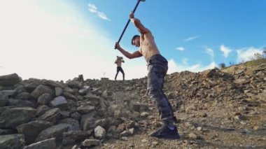 Sporcular Rocky Hill 'de fiziksel egzersiz yapıyorlar. Güçlü adam taş atan bir atletin arka planında büyük bir çekiçle taşları kırıyor. Yavaş çekim.