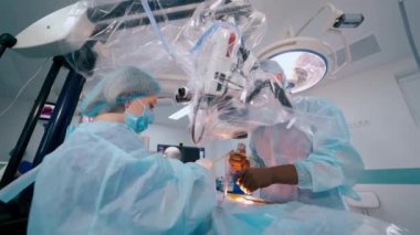 Cerrahi prosedür. Mikroskoba bakarken ameliyat yapan profesyonel bir doktor. Doktor üniformalı hemşire cerraha yardım ediyor..
