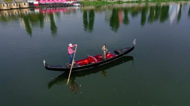 Gondolcu bir kadınla tekneye biniyor. Gün batımında nehir boyunca gondolla seyahat eden güzel bir bayan. Hava görüntüsü. Kamera hareketi.