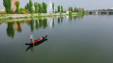 Gondol nehir boyunca yüzüyor. Kadın akşamları şehrin arka planında bir teknede eğleniyor. Hava görüntüsü. Kamera hareket ediyor.