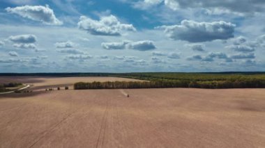Baharda doğanın panoramik görüntüsü. Mavi gökyüzünün altında tarımsal traktör çalışıyor. Traktör alana kimyasallar serpiyor. Hava görünümü.