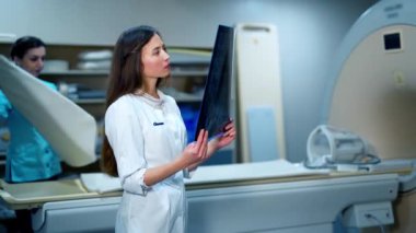 Röntgen taraması yapan profesyonel bir kadın doktor. Hastanedeki MRI makinesinin arka planındaki röntgen fotoğrafına bakan üniformalı genç bir kadın..