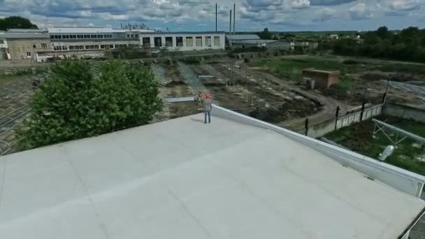 現場に太陽光発電所を建設する 平らな建物の屋上に立って 太陽電池パネルの取付けを見ている専門エンジニア エアリアルビュー — ストック動画