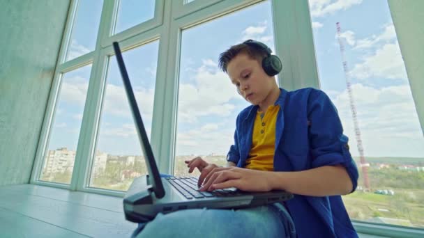 Подросток Наушниках Ноутбуком Окна Сконцентрированный Мальчик Нажимает Кнопки Ноутбуке Играя — стоковое видео