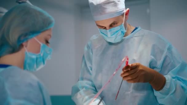 演劇における外科的プロセス 医療用制服とマスクの男性医師と女性アシスタントが病院で手術を行います — ストック動画