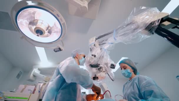 演劇における神経外科医 外科医は 病院で現代の顕微鏡を介して患者の手術を行います 下からの眺め — ストック動画