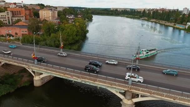 都市の橋で忙しい交通 川を渡る橋の上に車が移動する 船が水面に浮いている 空からの眺め スローモーション — ストック動画