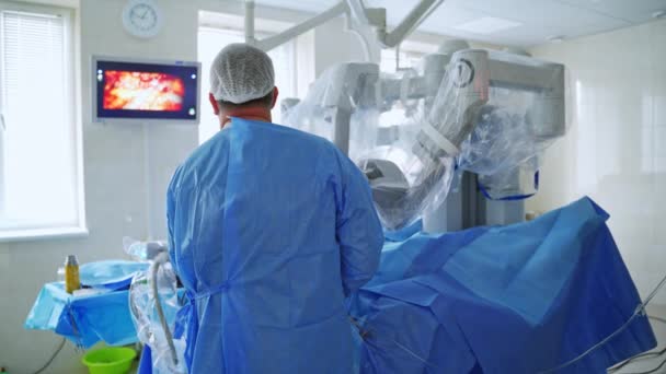 外科ロボットで手術をする医師 現代の診療所でロボット手術中にモニターを見ている外科医のバックビュー — ストック動画