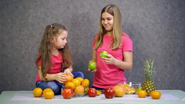母と娘は新鮮なフルーツで遊んでいました 小さな女の子とピンクのTシャツの女性がキッチンで一緒に時間を過ごしました テーブルの上の有機果物 — ストック動画
