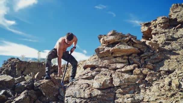 田径运动员在峡谷里用大锤操练 肌肉发达的男人站在岩石上 在蓝天下用大锤砸碎石头 慢动作 — 图库视频影像