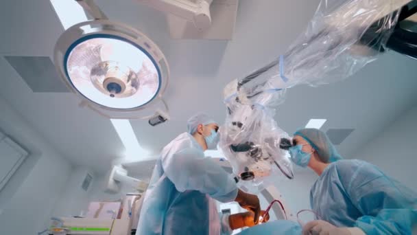 顕微鏡を介した現代の神経外科 スペシャリスト外科医は 軽い手術室で看護師と一緒に手術を行います 下からの眺め — ストック動画