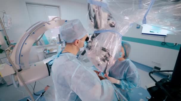 顕微鏡を介して手術を行うプロの医師と女性アシスタント 看護師は現代の手術室でプロの外科医を支援しています — ストック動画