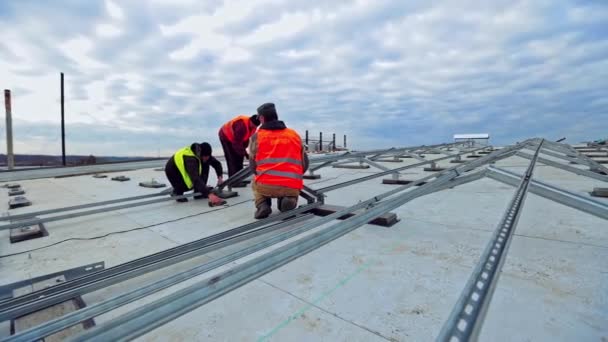 大きな建物の平らな屋根の上のソーラーパネル技術者 太陽光パネルの構築前に金属ベース 新しい太陽光発電所を設置する労働者 — ストック動画
