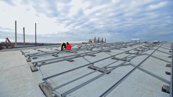 平らな屋根の将来の太陽電池パネルのための金属の基礎 美しい空の下で技術者による太陽電池パネル設置 新しい太陽光発電所の建設 — ストック動画