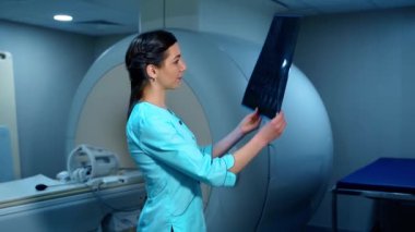 Doktor bir hastanın röntgen fotoğrafına bakıyor. MRI makinesinin arka planında x-ray resmini inceleyen kadın laboratuvar çalışanı.
