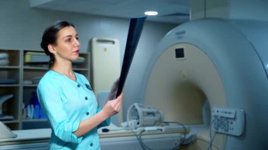 Röntgen fotoğrafında kadın uzman. MRI makinesinin arka planındaki görüntüye bakan bir kadın doktorun portresi.