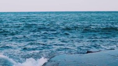 Dalgalar taş plajına çarpıyor. Deniz suyunun inanılmaz manzarası. Mavi su yüzeyi. Deniz suyunun güzel hareketi. Yavaş çekim.