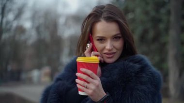 Açık havada çekici bir kız. Kürklü genç kadın parkta kahve içerken telefonla konuşuyor. Plastik bardaklı bir kadın portresi. Yavaş çekim.