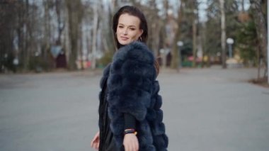 Kürk manto içinde güzel bir model. Güzel genç bayan parkta mutlu bir şekilde dönüyor. Kameranın önünde poz veren uzun siyah saçlı hoş bir kız..