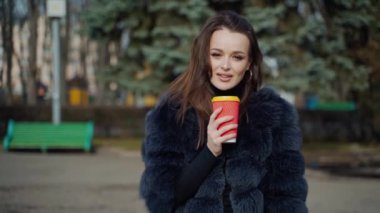 Açık havada bir modelin portresi. Plastik cam tutan kürklü zarif kadın parktaki kameraya bakıyor. Kahve içen alımlı kadının yüzü.