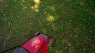 Bahçedeki çim biçme makinesi. Kadın yazın elektrikli çim biçme makinesiyle çim biçiyor. Bahçıvanlık süreci.