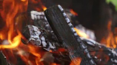 Kamp ateşinde odun yakmak. Yanan siyah ahşap üzerinde detaylı ateş hareketi. Parlak alevlerin içindeki tahta kütükler. Yakın plan..
