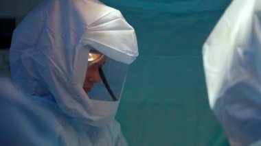 Koruyucu giysi konusunda uzmanlar. Doktorlar hastanede bir ameliyat yapıyorlar. Klinikte salgın sırasında güvenlik üniformalı bir cerrah..