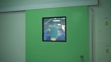 Hastanenin penceresinden ameliyat yapılıyor. Doktorların ekip çalışması bir hastaya ameliyat yapar. Koridor penceresinden yoğun bakım ünitesi..