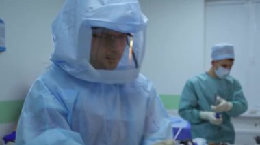 Cerrahların takım çalışması. Koruyucu giysili ve maskeli doktor ameliyathanede diğer tıp uzmanlarıyla birlikte bir ameliyat yapar..