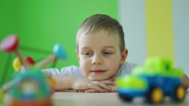 小さな男の子の顔 テーブルの上に頭を置いて 屋内でカラフルなおもちゃを見ている愛らしい子供 かわいい子供っぽい顔の肖像画 クローズアップ — ストック動画