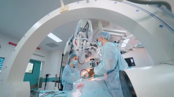 手術室には外科医と看護師がいる 患者は外科のテーブルで麻酔を受けています 神経外科の間に現代装置を使用する専門家 — ストック動画