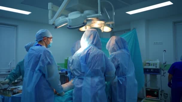 手術室にいる医師 明るい医療ランプの下で操作を行う医療ユニフォームの専門外科医のチーム — ストック動画