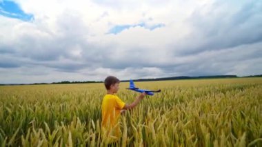 Tarım arazisindeki küçük çocuk. Sarı tişörtlü çocuk elinde oyuncak bir uçakla sahada uçuyormuş gibi yapıyor. Yaz mevsiminde tarımsal tesislerdeki çocuk.