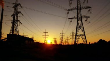 Aktarım kuleleri turuncu gün batımında. Elektrik direkleri. Yüksek voltajlı elektrik direğinden batan güneşe doğru hareket ediyor. Enerji verimliliği kavramı.