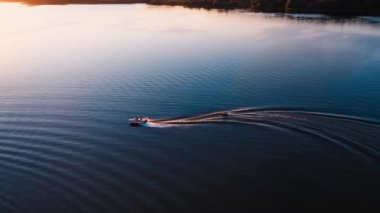 Gün batımında sudaki sürat teknesi. İki tekneyle akşam nehrinin panoramik manzarası. Motorlu tekne insanlarla küçük bir tekne çekiyor. Yukarıdan görüntüle.