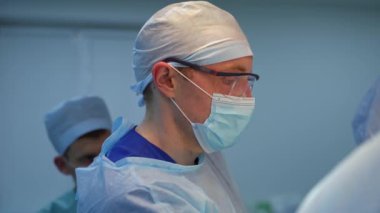 Cerrahların takım çalışması. Tıbbi maskeli ve gözlüklü doktor. Koruyucu giysiler içinde bir grup sağlık çalışanı bir operasyon gerçekleştiriyor..
